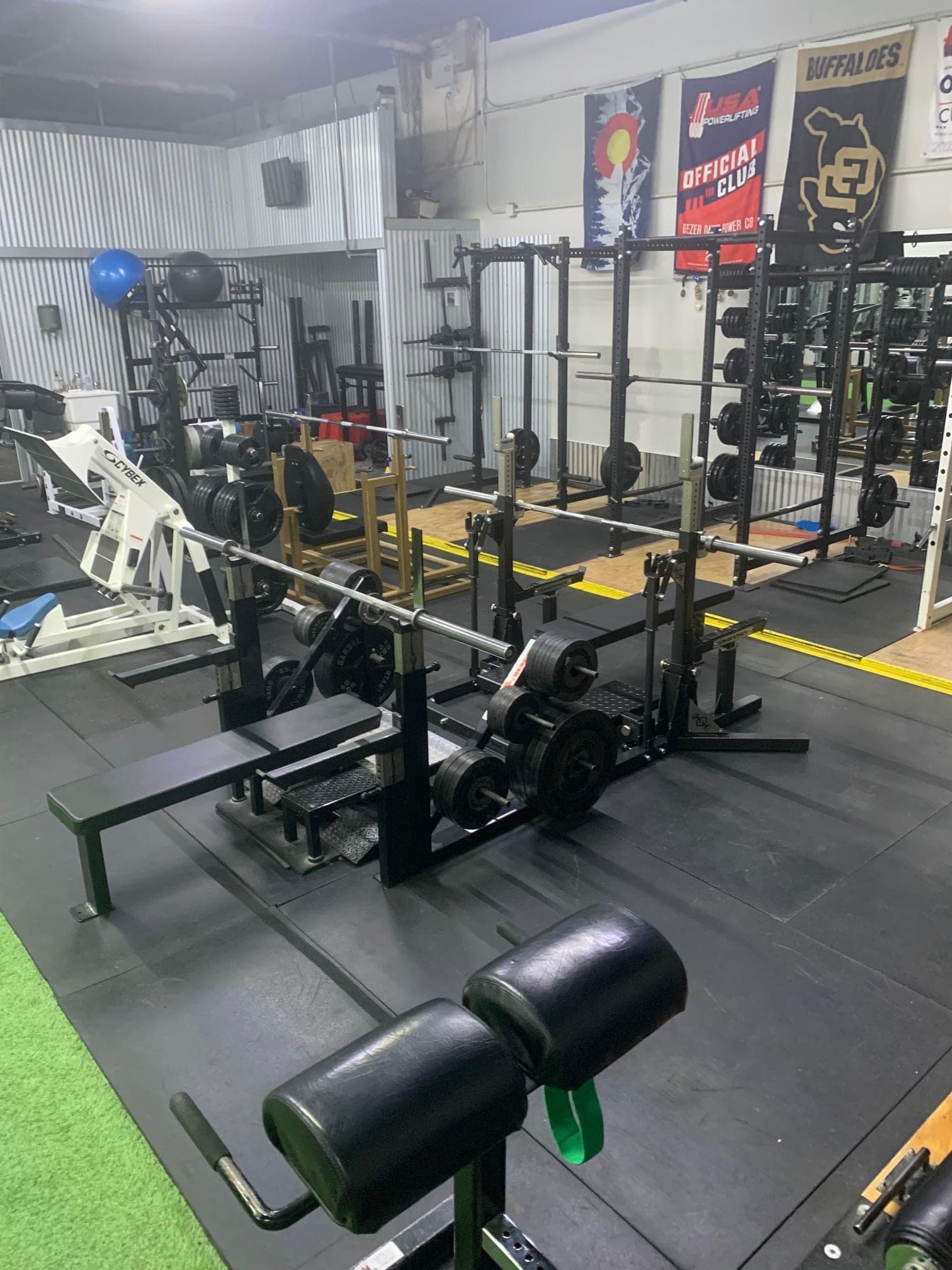 CNE's weight room with power racks, plate trees, and club banners on the wall